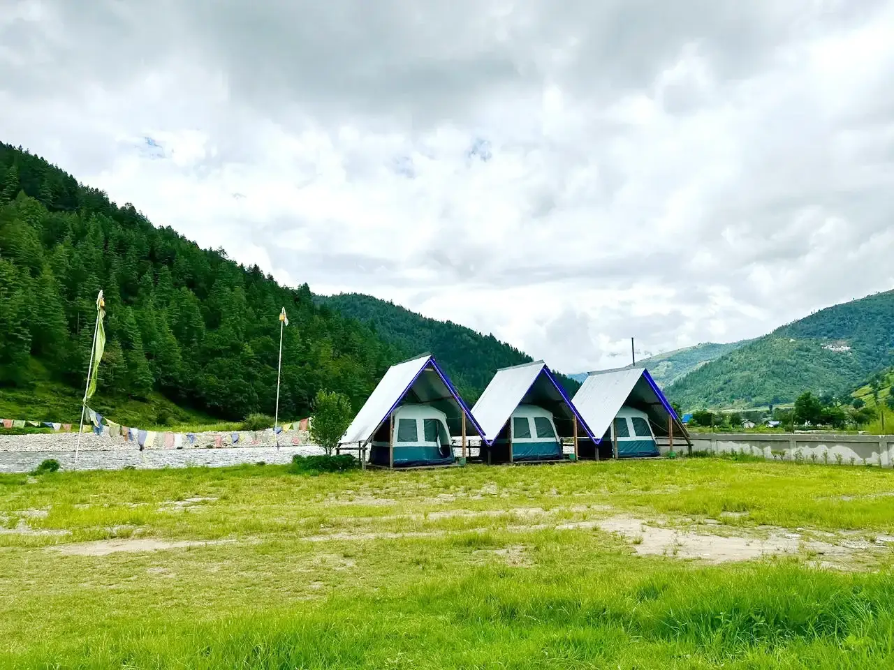 Three A-frame tents in open field with mountain backdrop at Sangti Valley
